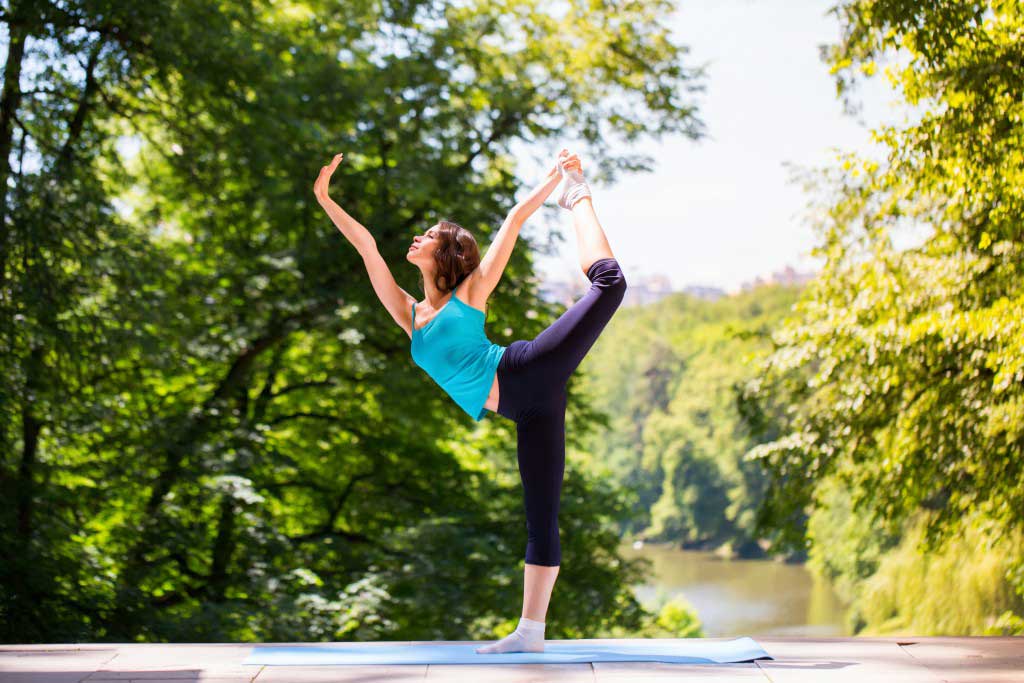 woman doing advanced yoga in a park near a river