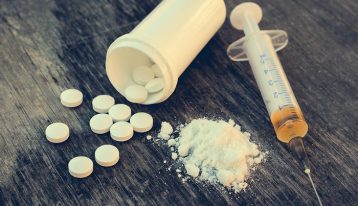 Numerous states are filing lawsuits against drug manufacturers as a result of the epidemic and the financial tax it has created for these government organizations, white pills spilling out of bottle - white powder - syringe full of drugs