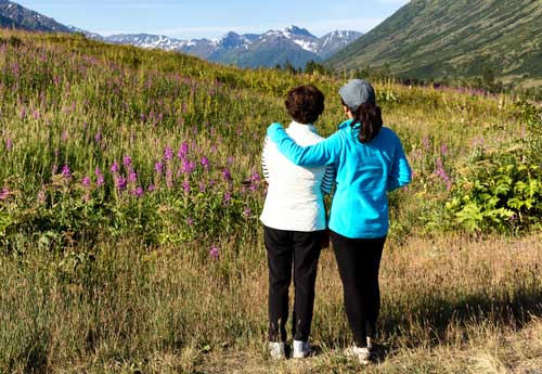 grown daughter with arm around mother's shoulder looking out into mountain scenery