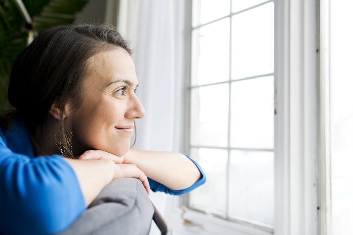 smiling woman looking out house window - transitional