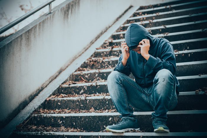 man sitting in hooded sweatshirt on stairs outdoors, visibly upset - spouse addicted