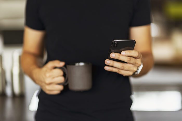 man holding a cup of coffee and dialing cell phone - pay for addiction treatment