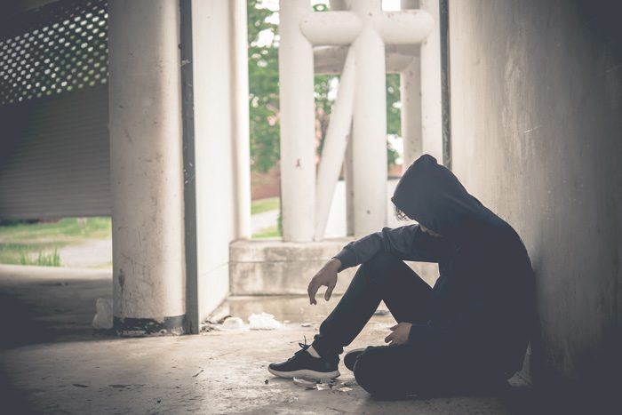 young man in hoodie sitting on floor of abandoned house or building, with syringes and heroin paraphernalia - heroin addiction, Methamphetamine Addiction Treatment in Texas