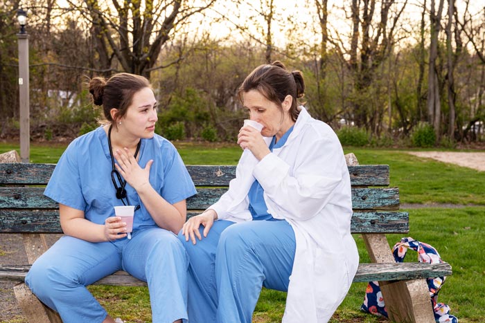 two female healthcare workers talking on a bench outside - healthcare workers