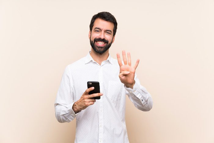 What Are the Benefits of Inpatient Treatment?, Benefits of Inpatient Treatment, handsome, smiling man holding his cell phone and using his other hand to signal the number four - inpatient treatment